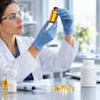 Female scientist examining golden liquid sample in laboratory with pharmaceutical research equipment and data analysis
