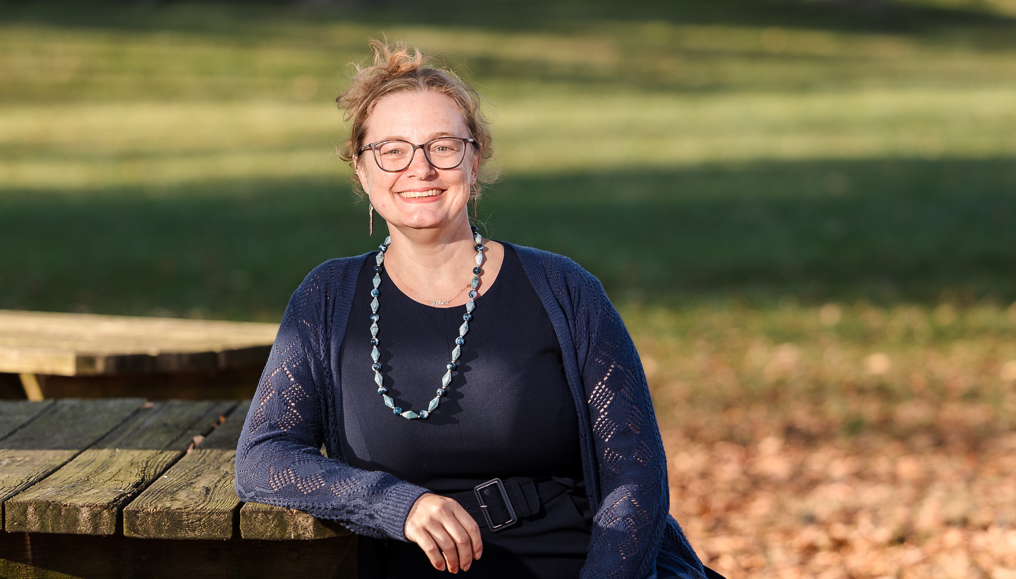 Woman wearing glasses and dark cardigan smiling at camera outdoors