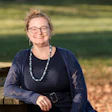 Woman wearing glasses and dark cardigan smiling at camera outdoors