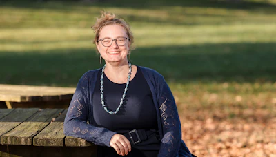 Woman wearing glasses and dark cardigan smiling at camera outdoors