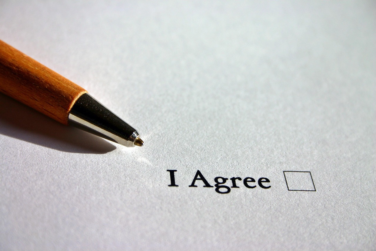 Wooden pen positioned above 'I Agree' text with empty checkbox on white paper