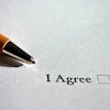 Wooden pen positioned above 'I Agree' text with empty checkbox on white paper