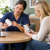 Healthcare provider in blue scrubs discussing medication with patient holding smartphone, accompanied by golden retriever
