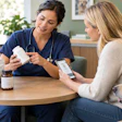Healthcare provider in blue scrubs discussing medication with patient holding smartphone, accompanied by golden retriever