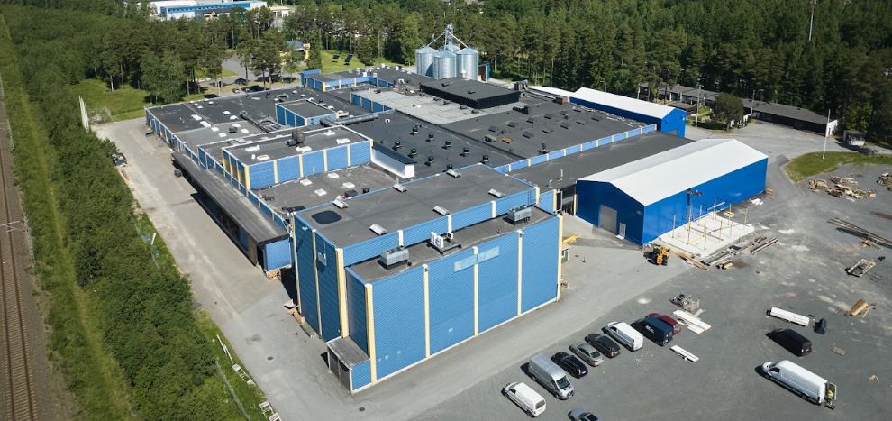 Aerial view of blue and white industrial storage facility with multiple units, parking area, and surrounding forest