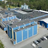 Aerial view of blue and white industrial storage facility with multiple units, parking area, and surrounding forest