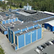 Aerial view of blue and white industrial storage facility with multiple units, parking area, and surrounding forest