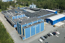 Aerial view of blue and white industrial storage facility with multiple units, parking area, and surrounding forest