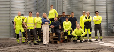 Team of workers in high-visibility safety gear standing together in front of industrial metal building